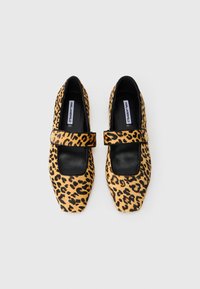 Leoparda raksta dzīvokļi ar melnu kvadrātveida purngali un siksniņu, izgatavoti no faktūras materiāla. Iespēja ir eleganta dizaina un kontrastējošu krāsu akcentu.