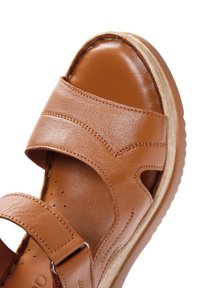 Sandal in pelle marrone con fasce larghe, texture liscia e soletta imbottita. Caratterizzato da una suola in legno chiaro e cuciture decorative.