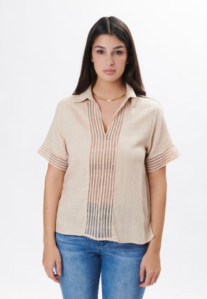 Camicia in lino color beige chiaro con maniche corte, scollatura a V e dettagli decorativi intricati al centro e lungo i polsini.