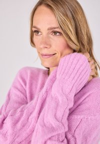 Helles rosa Sweatshirt mit lockerer Passform, gerippten Bündchen und einem strukturierten, weichen Strick. Das Design umfasst ein Zopfmuster.