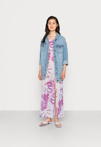 Jaqueta de ganga, azul clara, de corte oversized; vestido maxi com padrão floral rosa e uma fenda; sandálias brancas com um design simples e um ligeiro salto.