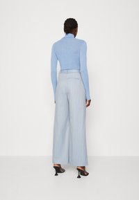 Lichtblauw getailleerd langemouwen top, gecombineerd met lichtblauwe high-waisted broek met streepjes en zwarte hakken.