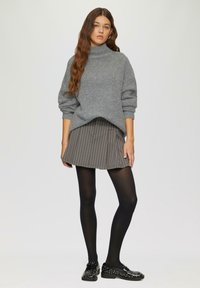 Grauer Strickpullover mit hohem Kragen, kombiniert mit einem schwarz-weiß gestreiften Rock, schwarzen Strumpfhosen und schwarzer genagelter Slipper.