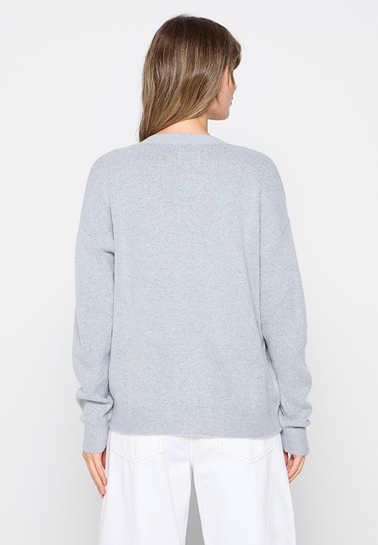 Maglione lavorato a maglia grigio chiaro con una vestibilità ampia, scollatura rotonda e spalle abbassate. Polsini e orlo a coste. Tessuto semplice, senza motivi visibili.