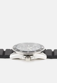 Montre de plongée noire avec un boîtier en acier inoxydable, une lunette ronde et un bracelet en caoutchouc texturé. Elle possède un cadran noir et des index argentés.