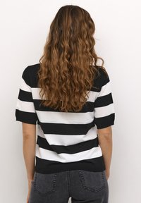 Pull à manches courtes noir et blanc à rayures, avec une coupe décontractée, une texture lisse et un ourlet côtelé. Associé à un jean gris foncé taille haute.