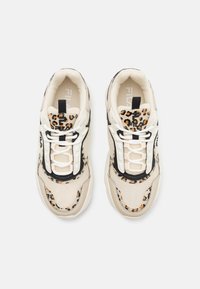 Beige tenisice s robusnim dizajnom, koje sadrže nijanse leopard uzorka, crne preklopke i bijele vezice na teksturiranoj površini.