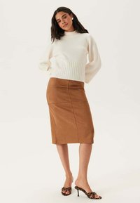 Pull en tricot blanc texturé avec des manches ballon associé à une jupe midi en cuir synthétique marron ajustée, présentant une finition lisse et des détails de couture.