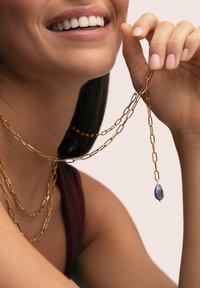 Collar de cadena de oro con eslabones entrelazados, que presenta un colgante con una piedra preciosa azul colgante. Textura suave y diseño en capas.