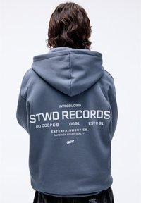 Sudadera con capucha de tela gris que presenta un gran gráfico blanco en la parte posterior con el texto "STWD RECORDS" y detalles adicionales debajo.