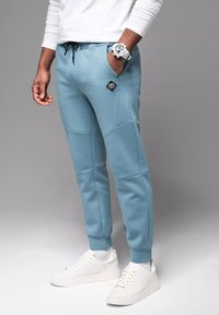 Jasnoniebieskie spodnie dresowe z miękkiego materiału, z czarną naszywką z logo, elastycznym pasem, bocznymi kieszeniami i prążkowanymi mankietami.