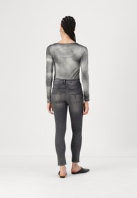 Haut à manches longues gris à motifs avec un col rond, associé à un jean skinny gris foncé, présentant une légère décoloration et des poches arrière.