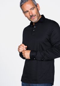 Schwarzes Langarm-Polohemd mit Kragen, Drei-Knopf-Leiste und kontrastierenden schwarzen Bündchen. Hergestellt aus glattem Stoff mit seitlichen Schlitzen.