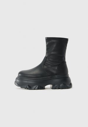 Black mid-calf boot with smooth leather upper and thick, sculpted chunky sole with deep tread pattern.
