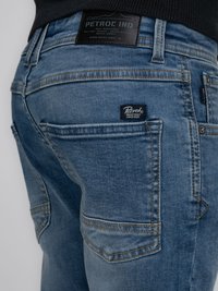 Jeans de denim azul con un acabado desgastado, que presentan múltiples bolsillos, costuras naranjas y una etiqueta de cuero negro en la cintura.