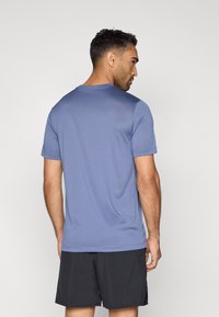 Ανδρικό πουκάμισο κοντομάνικο σε απαλό, ανοιχτό μπλε ύφασμα με στρογγυλή λαιμόκοψη και ομαλή υφή, συνδυασμένο με μαύρες βερμούδες.