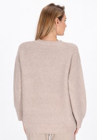 Pullover tricotat bej cu guler rotund, umeri lăsați și manșete cu dungi. Textura este moale și voluminoasă, oferind o croială relaxată.