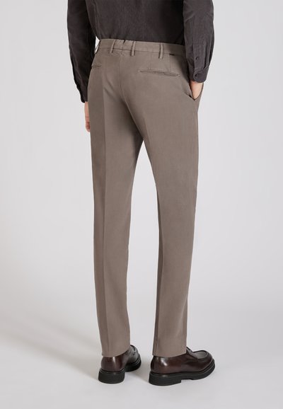 Jasnobrązowe spodnie wykonane z gładkiego materiału, o dopasowanym kroju, z tylnymi kieszeniami i kieszeniami bocznymi. Noszone z ciemnymi butami.