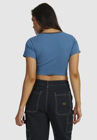 Afskåret blå ribbet t-shirt med korte ærmer, med rund halsudskæring og sort kant, parret med sorte bukser og synlige sømdetaljer.