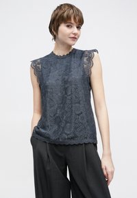 Mežģīņu tops tumši pelēkā krāsā ar smalkiem ziedu rakstiem, viļņotām malām un īsām piedurknēm. Kombinēts ar brīvi pieguļošām pelēkām biksēm.