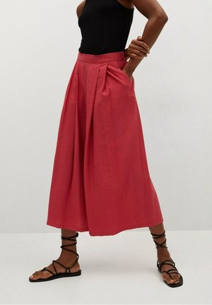 Pink culotte-style pants with pleats and a high waist, made of lightweight fabric. Paired with black strappy sandals.