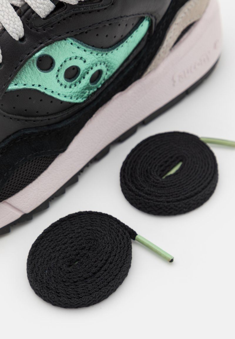 Detail eines schwarzen und teal Sportschuhs mit zwei coiled schwarzen Schnürsenkeln auf einem weißen Hintergrund.
