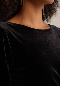 Black velvet top with a boat neckline and soft texture. Includes subtle seam detailing and hangs loosely on the shoulders.