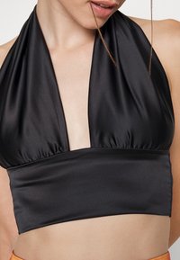 Svart halterneck croptop i slätt satinmaterial, med en djup V-ringning och rynkdetaljer runt bysten.