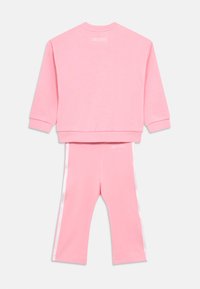 Ροζ φούτερ και αντίστοιχο παντελόνι φόρμας, κατασκευασμένα από απαλό ύφασμα, με λευκές ρίγες στα πλάγια και ένα λογότυπο στο πίσω μέρος.