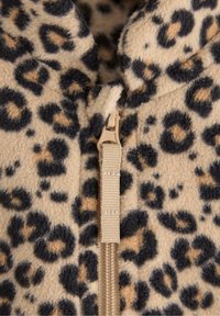 Fleecetakki, jossa on vaaleanruskea pohja mustalla ja ruskealla leopardikuviolla, ja sitä täydentää beige vetoketju sekä tekstuuri.