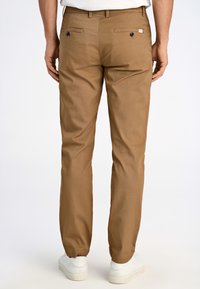 Bruna byxor med tapered passform, tillverkade av lättviktigt material. Har elastiska muddarf och två bakfickor med svarta knappar.