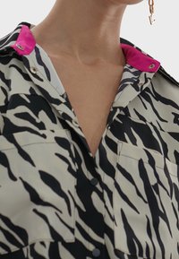 Short-sleeve shirt featuring a black and white zebra print, with a bright pink collar. Buttons along the front and two chest pockets.
