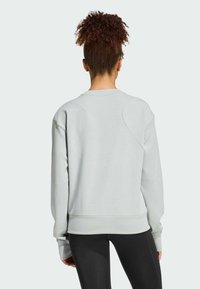 Jasnoszara bluza z miękkiego materiału, o luźnym kroju, okrągłym dekolcie i opadających szwach na ramionach. W zestawie z czarnymi legginsami.