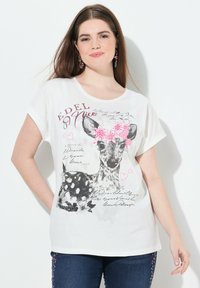 Camiseta blanca con un gráfico de ciervo en blanco y negro, adornado con acentos florales en rosa y texto. Manga corta, corte relajado.