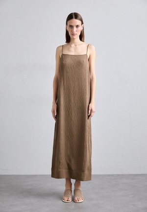 Robe midi marron texturée avec de fines bretelles, dotée d'un décolleté carré. Associée à des sandales tressées beiges, sur un fond neutre.