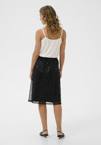 Falda de encaje negro con un patrón intrincado, superpuesta a un forro suave; combinada con una blusa blanca de tirantes finos y ligera.