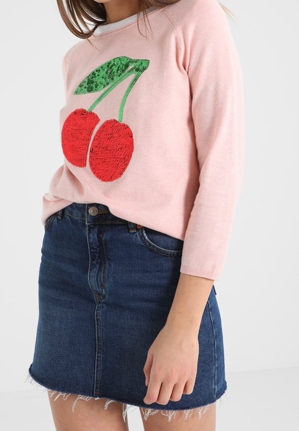 Rosa tröja med gröna och röda körsbärsbroderier, tillsammans med en jeanskjol med fransad kant och framknäppning.