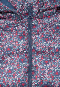 Tela de color azul acolchada con corazones rojos y pequeñas flores rojas, rosas y blancas, con un cierre central de color marino y botones de presión.