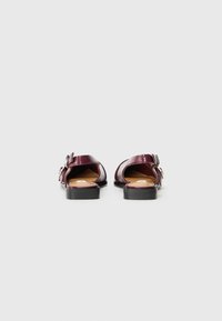 Burgundy leather sandals with open back, rounded toe, flat black sole, and decorative buckle detail on the side.
