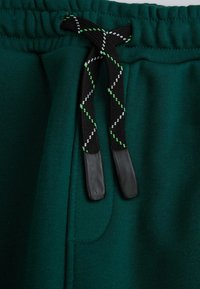 Zielone dresowe spodnie z polaru mają czarny sznurek do ściągania w białe i zielone wzory w diamenty, z plastikowymi końcówkami. Pas jest elastyczny.