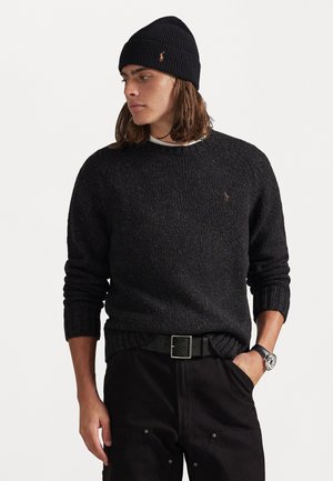 Must mustan villane sviiter ribatud varrukatega ja ümar kaelus, koos musta beanie'ga. Kitsad mustad püksid ja hõbedast randme kell annavad komplektile viimase viimistluse.