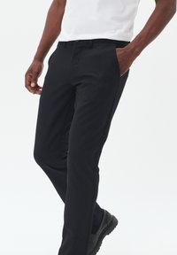 Zwarte broek met een getailleerde pasvorm, voorzien van zijzakken en een gladde, matte textuur. Draag het met een wit shirt en donkere schoenen.