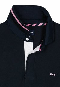 Polo shirt de couleur marine avec un plastron avant blanc, un col doublé de rose, et un petit détail de logo sur la poitrine.