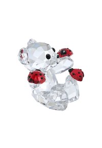 Kryštálová figúrka medveďa, ktorý drží dve červené lienky. Má facétované povrchy, priehľadný materiál a čierne oči, pričom predvádza jemné detaily.