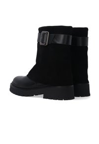 Schwarze Knöchelschuhe aus Wildleder, mit einem Lederriemen und einer Schnalle sowie einer klobigen, strukturierten Sohle für zusätzlichen Halt und Stabilität.
