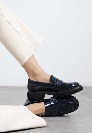 Mocasines de charol marino con una suela negra gruesa, que presentan detalles de costura y una correa decorativa en la parte superior.