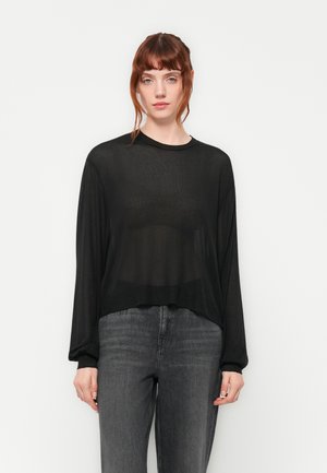 Svart gjennomsiktig langermet topp med rund hals, avslappet passform og subtil tekstur, paired med mørkegrå jeans.