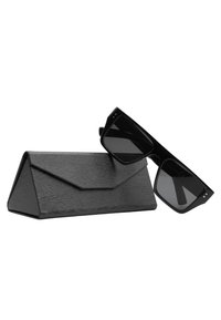 Occhiali da sole neri con lenti quadrate, realizzati in plastica, posti accanto a un astuccio triangolare nero testurizzato con un motivo in rilievo.