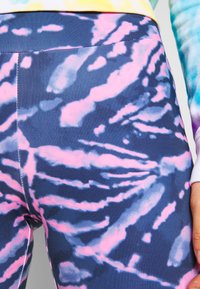 Leggings od rastezljivog materijala imaju tamnoplavu podlogu s roza i svijetloplavim tie-dye uzorcima. Elastični pojas je gladak, a šavovi su vidljivi.