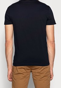 Musta puuvillapaita lyhyillä hihoilla, pyöreä pääntie, sileä pinta ja siisti takasuunnittelu. Yhdistetty beigeihin housuihin.